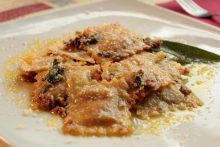 Ravioli di salsiccia e patate, menta, timo e erba cipollina conditi al piatto con burro, salvia e salsiccia sminuzzata